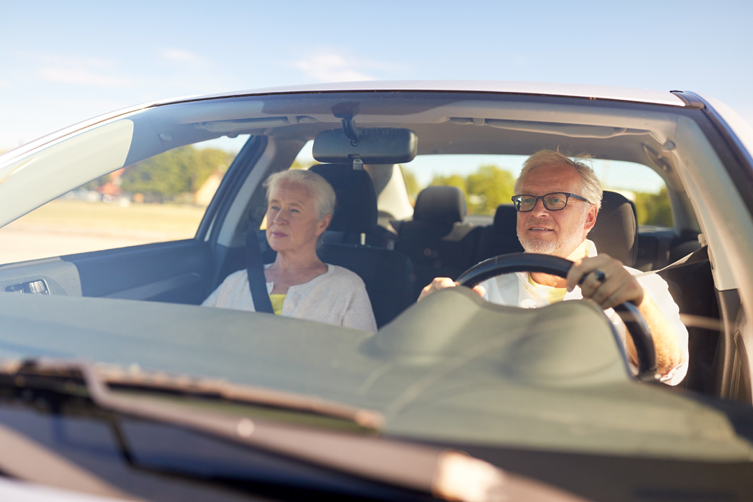 Възрастни мъж и жена се возят в автомобил през деня
